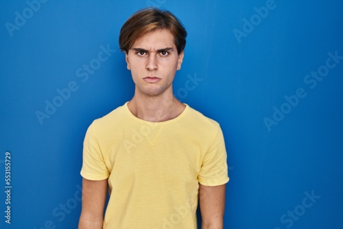 Young man standing over blue background skeptic and nervous, frowning upset because of problem. negative person.