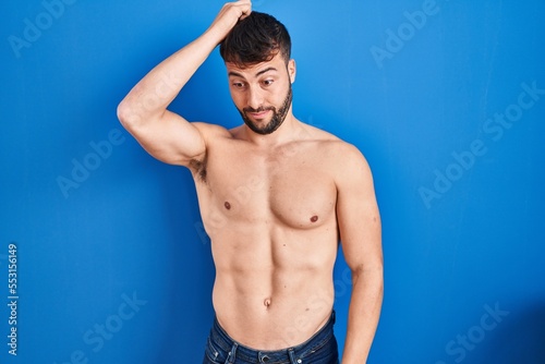 Handsome hispanic man standing shirtless confuse and wonder about question. uncertain with doubt, thinking with hand on head. pensive concept.