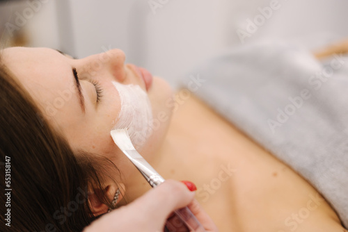 Cosmetologist applying clay mask on woman's face in spa salon. First person view of male face during procedure.