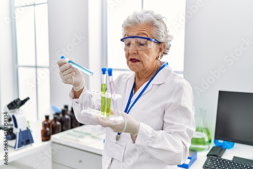 Senior grey-haired woman wearing scientist uniform holding test tubes at laboratory