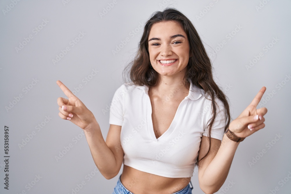 Young teenager girl standing over white background smiling confident pointing with fingers to different directions. copy space for advertisement Young teenager girl standing over white background smiling confident pointing with fingers to different directions. copy space for advertisement