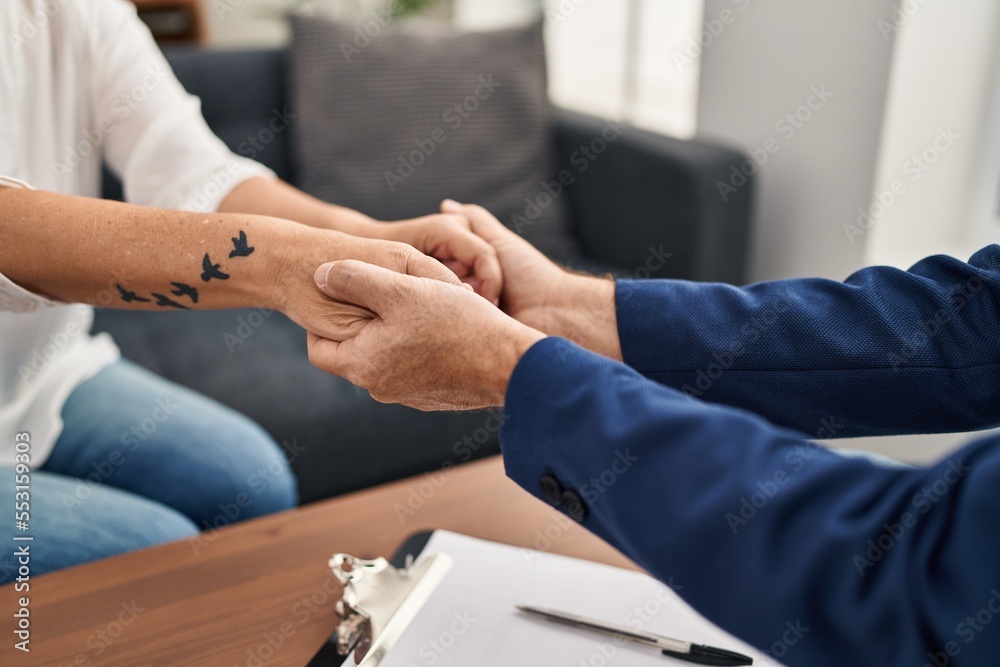 Obraz premium Middle age man and woman pshychologist and patient consueling holding hands at psychology center
