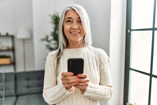Middle age grey-haired woman smiling confident using smartphone at home