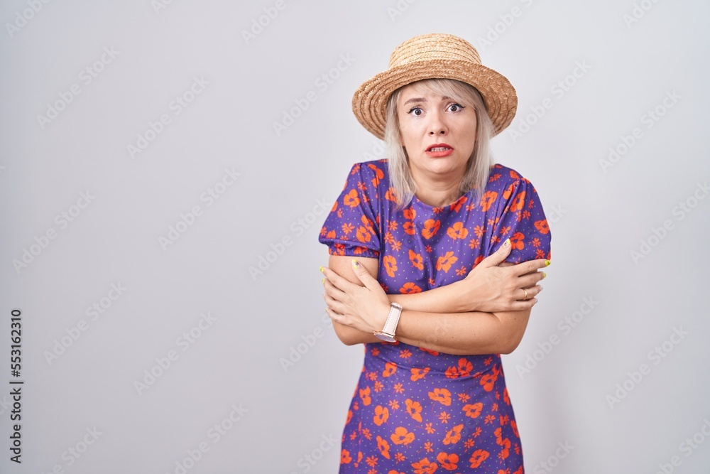 Young caucasian woman wearing flowers dress and summer hat shaking and freezing for winter cold with sad and shock expression on face Young caucasian woman wearing flowers dress and summer hat shaking and freezing for winter cold with sad and shock expression on face