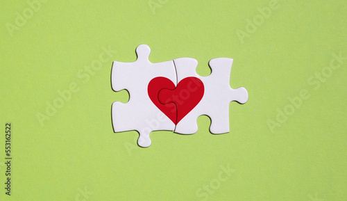 concept and metaphor of the love union of two people. two white puzzle pieces with a red heart on a green background.