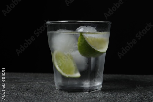 Glass of vodka with lime slices and ice on grey table