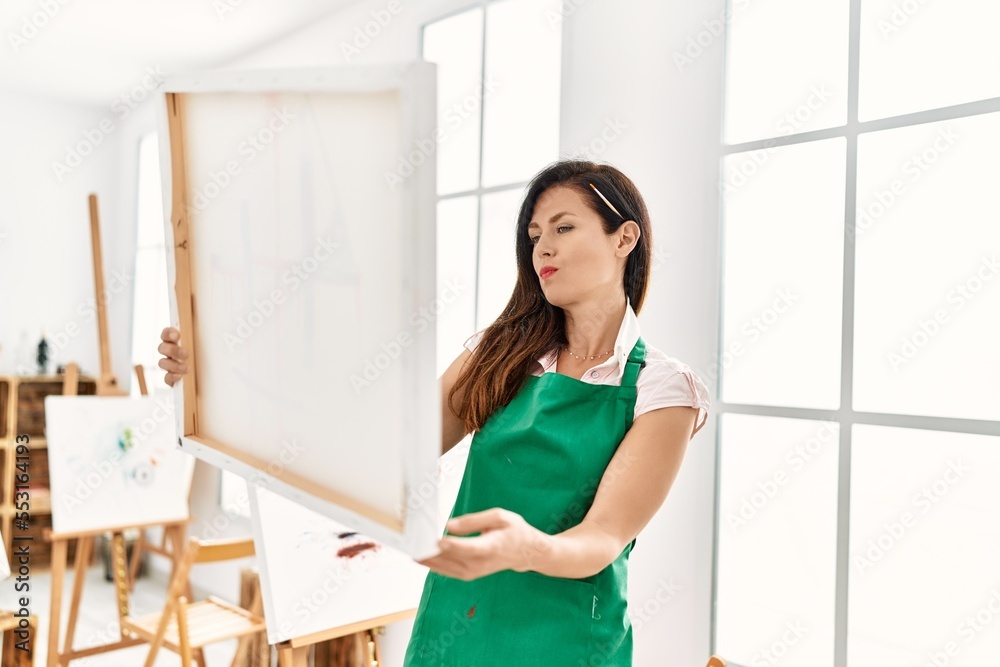 Middle age hispanic woman holding canvas draw at art studio Middle age hispanic woman holding canvas draw at art studio