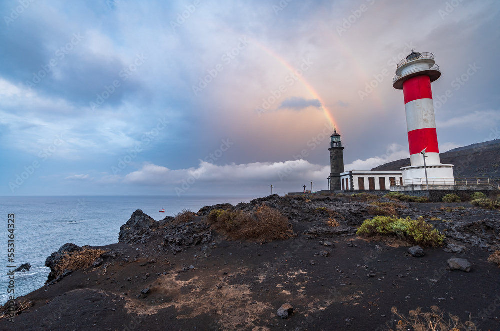 Rough volcanic coastline with old and new lighthouses under the rainbow