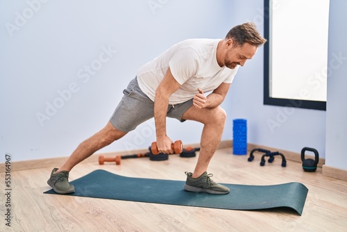 Young caucasian man smiling confident using dumbbell training at sport center