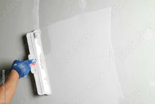 Professional worker plastering wall with putty knife, closeup photo