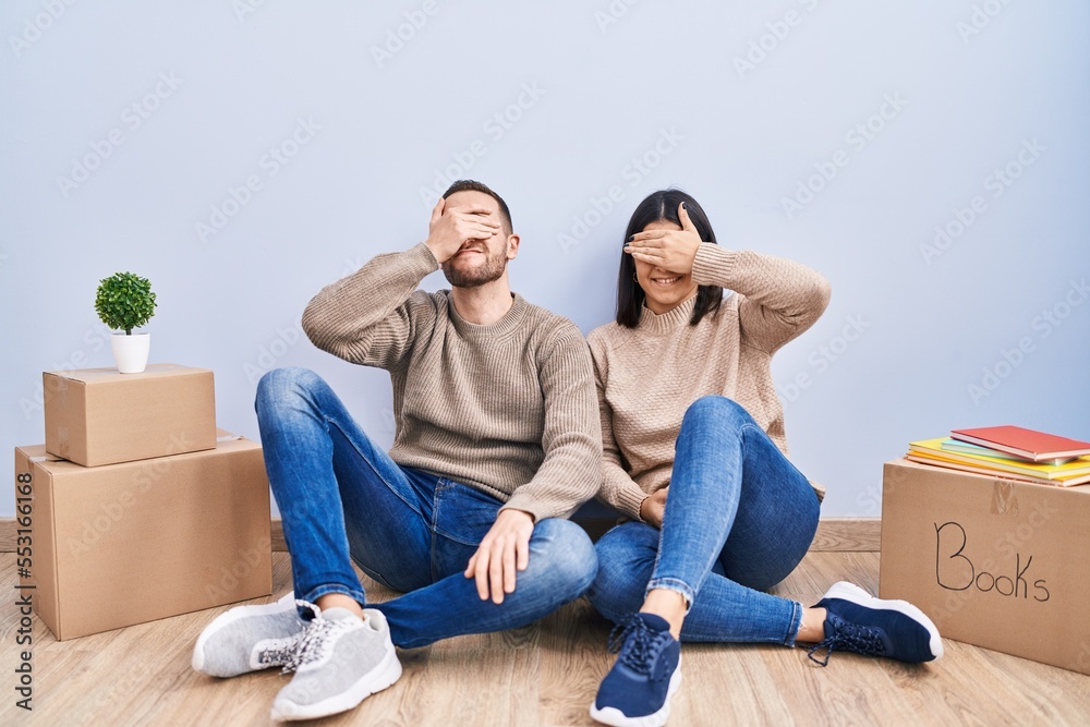 Young couple moving to a new home smiling and laughing with hand on face covering eyes for surprise. blind concept. Young couple moving to a new home smiling and laughing with hand on face covering eyes for surprise. blind concept.