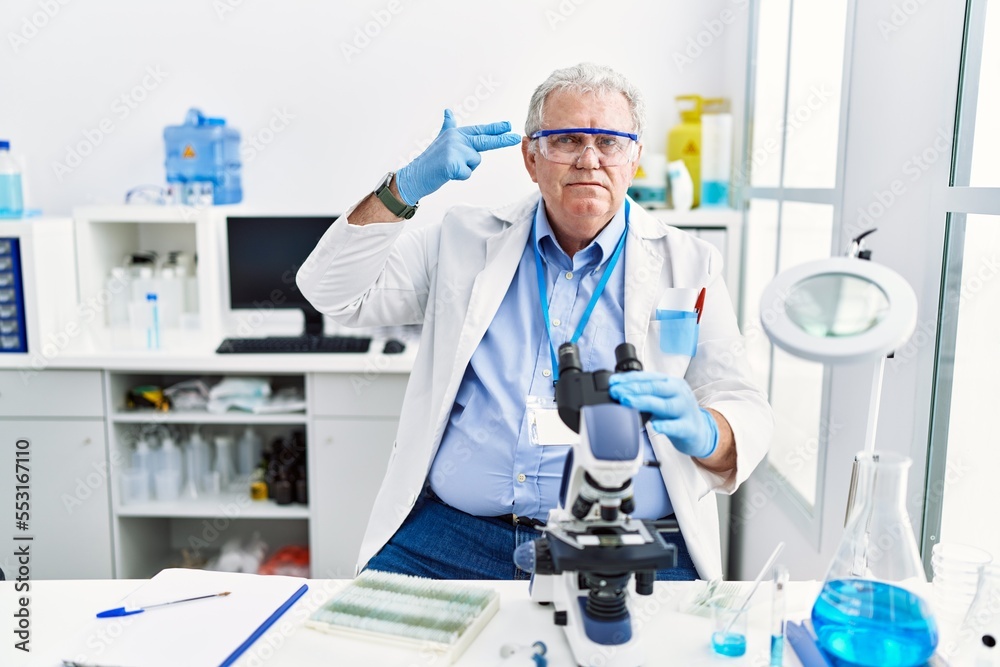 Senior caucasian man working at scientist laboratory shooting and killing oneself pointing hand and fingers to head like gun, suicide gesture. Senior caucasian man working at scientist laboratory shooting and killing oneself pointing hand and fingers to head like gun, suicide gesture.