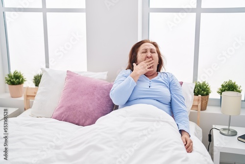 Senior woman sitting on bed yawning at bedroom