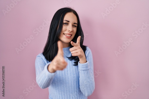 Hispanic woman standing over pink background pointing fingers to camera with happy and funny face. good energy and vibes.