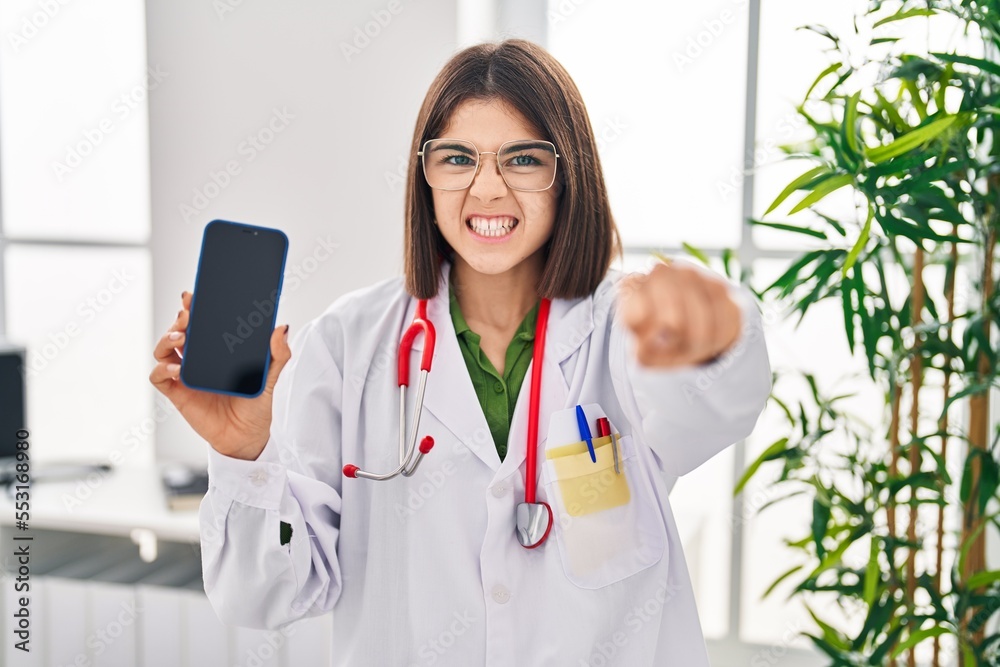 Young hispanic doctor woman showing smartphone screen annoyed and frustrated shouting with anger, yelling crazy with anger and hand raised Young hispanic doctor woman showing smartphone screen annoyed and frustrated shouting with anger, yelling crazy with anger and hand raised