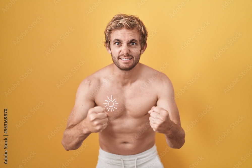 Caucasian man standing shirtless wearing sun screen angry and mad raising fists frustrated and furious while shouting with anger. rage and aggressive concept.