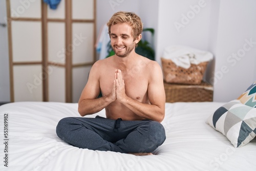 Young man sitting on sofa doing yoga exercise at bedroom