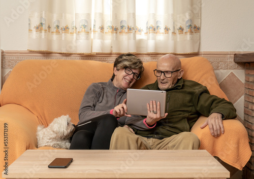 Padre con su hija haciendo videollamada al nieto, persona mayor con su hija sentado en el sillón de casa