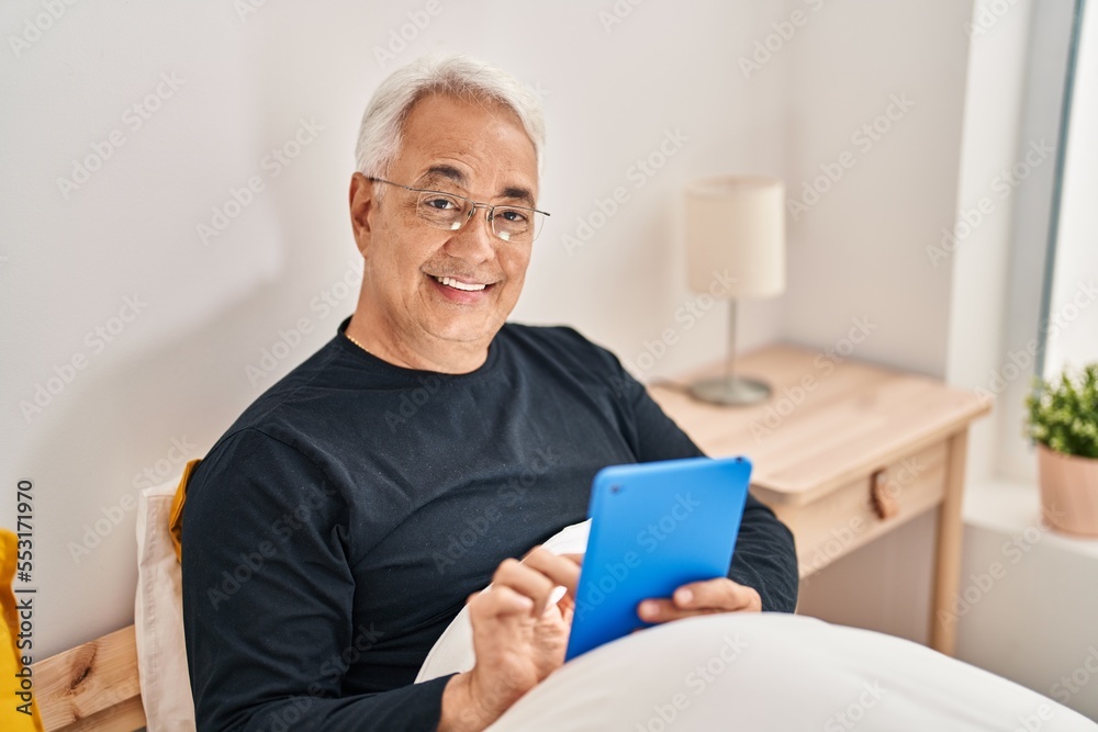 Senior man using touchpad sitting on bed at bedroom Senior man using touchpad sitting on bed at bedroom