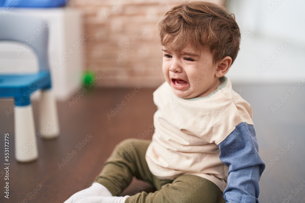 Adorable hispanic toddler sitting on floor crying at home