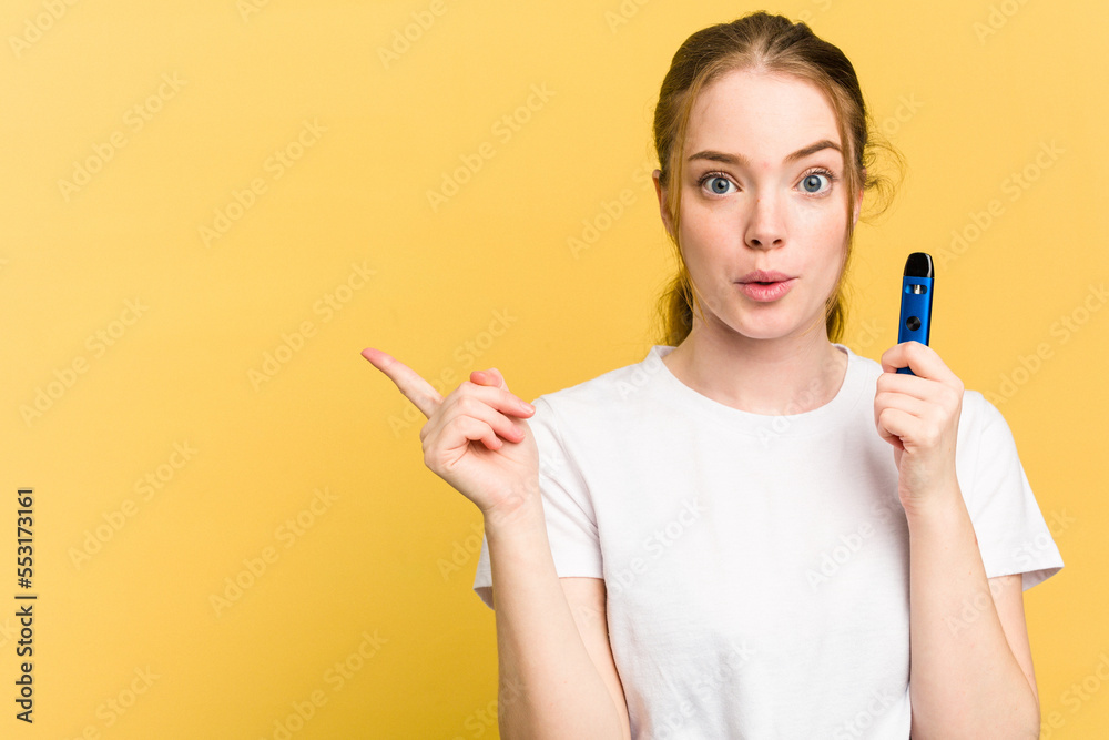 Young cute woman holding a vaper isolated on yellow background pointing to the side Young cute woman holding a vaper isolated on yellow background pointing to the side