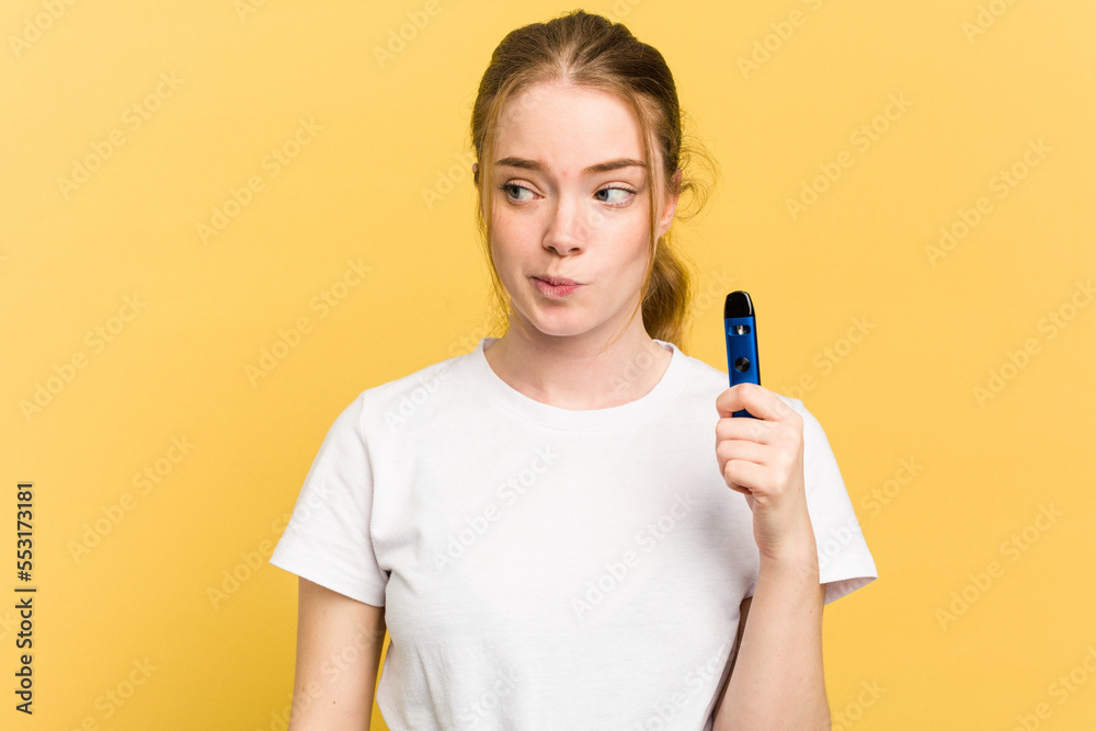 Young cute woman holding a vaper isolated on yellow background confused, feels doubtful and unsure. Young cute woman holding a vaper isolated on yellow background confused, feels doubtful and unsure.