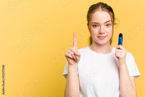 Young cute woman holding a vaper isolated on yellow background showing number one with finger.