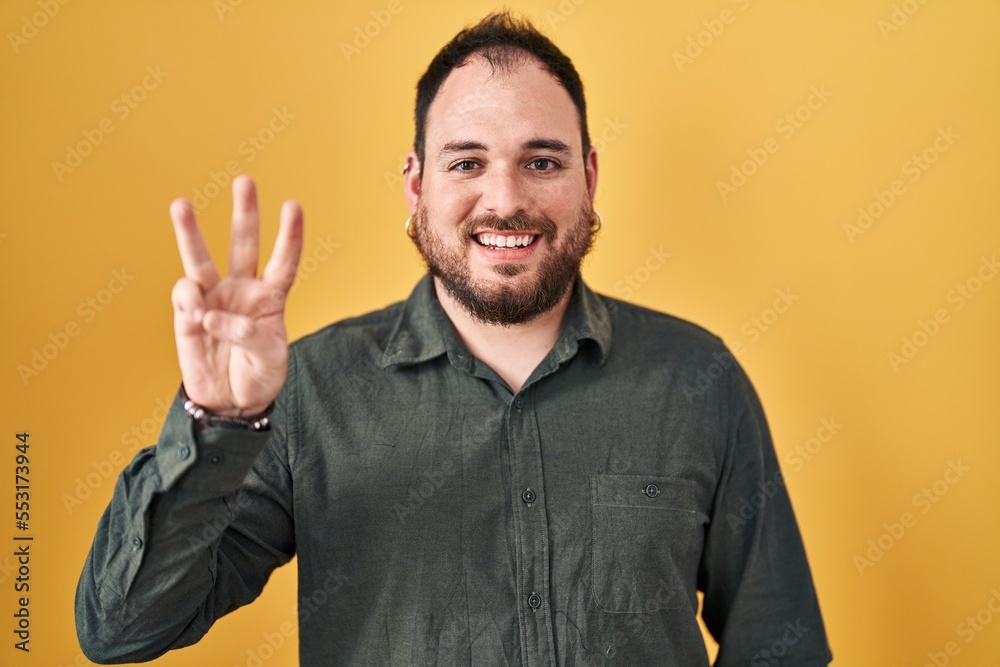 Plus size hispanic man with beard standing over yellow background showing and pointing up with fingers number three while smiling confident and happy. Plus size hispanic man with beard standing over yellow background showing and pointing up with fingers number three while smiling confident and happy.
