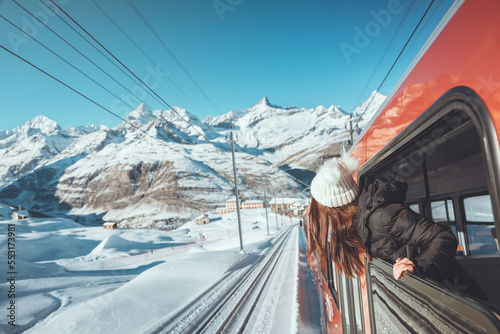 Happy woman traveler looks out from window traveling by train in beautiful winter mountains, Travel concept.