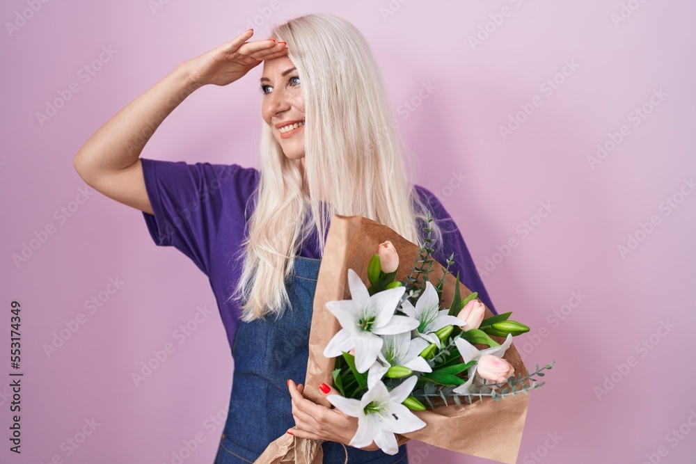 Caucasian woman holding bouquet of white flowers very happy and smiling looking far away with hand over head. searching concept.