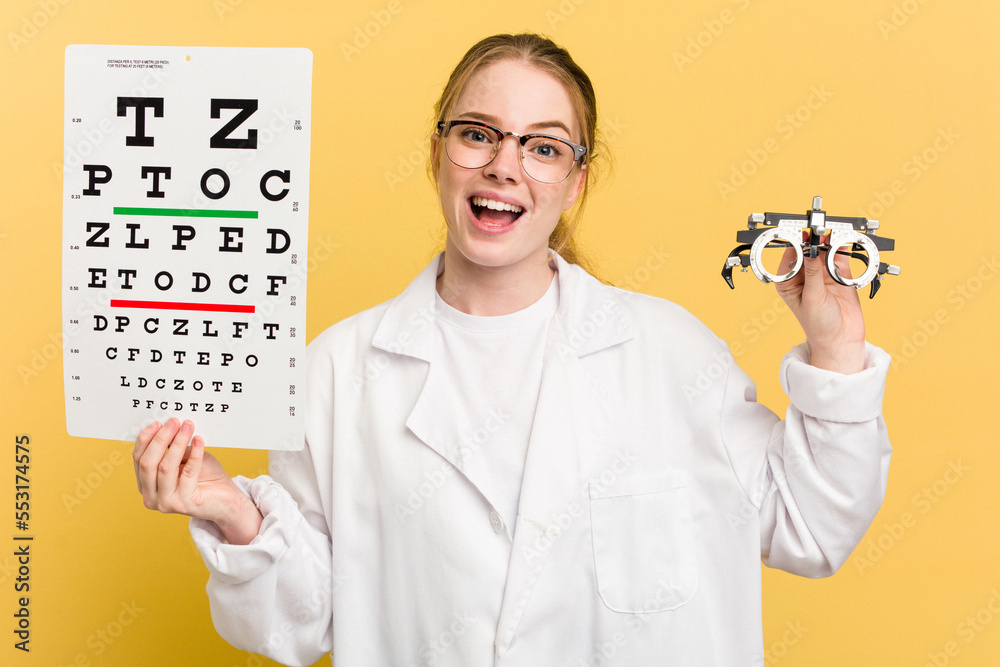 Young caucasian oculist woman doing a eye exam isolated on yellow background Young caucasian oculist woman doing a eye exam isolated on yellow background