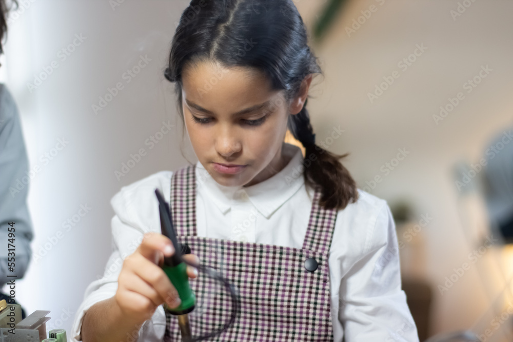 Portrait of serious schoolgirl making robotics. Concentrated girl rigging up circuit board. Education, hobby or technology concept Portrait of serious schoolgirl making robotics. Concentrated girl rigging up circuit board. Education, hobby or technology concept