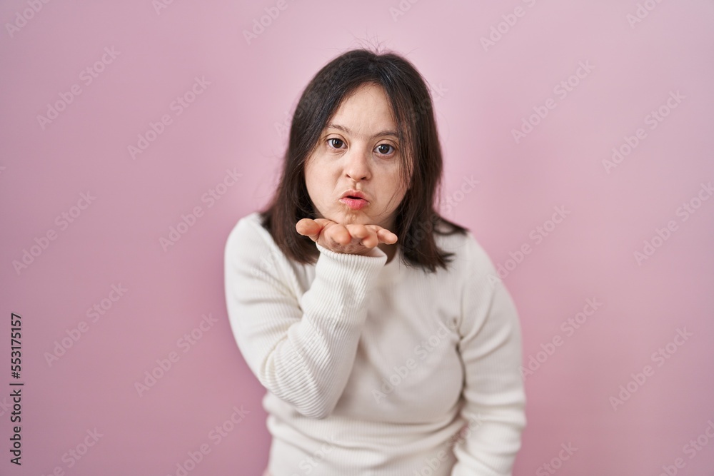 Woman with down syndrome standing over pink background looking at the camera blowing a kiss with hand on air being lovely and sexy. love expression. Woman with down syndrome standing over pink background looking at the camera blowing a kiss with hand on air being lovely and sexy. love expression.