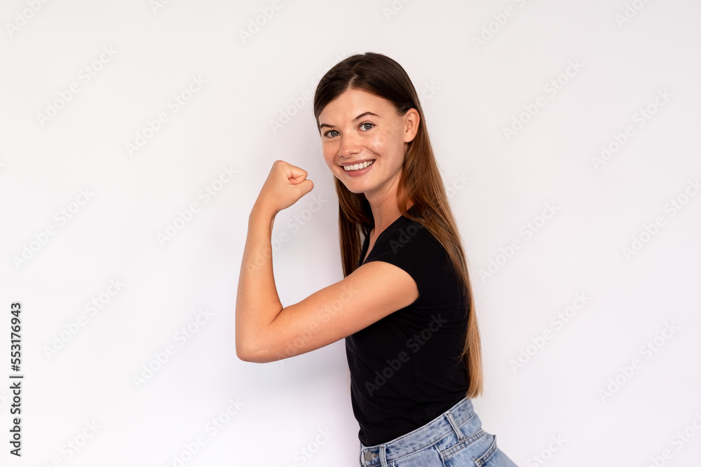 Portrait of happy young woman showing bicep on white background. Caucasian lady wearing black T-shirt and jeans showing strength and fit body. Fitness and power concept Portrait of happy young woman showing bicep on white background. Caucasian lady wearing black T-shirt and jeans showing strength and fit body. Fitness and power concept
