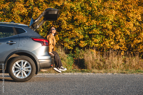 There is a woman sitting in the trunk of a car enjoying the sun as she enjoys the warmth