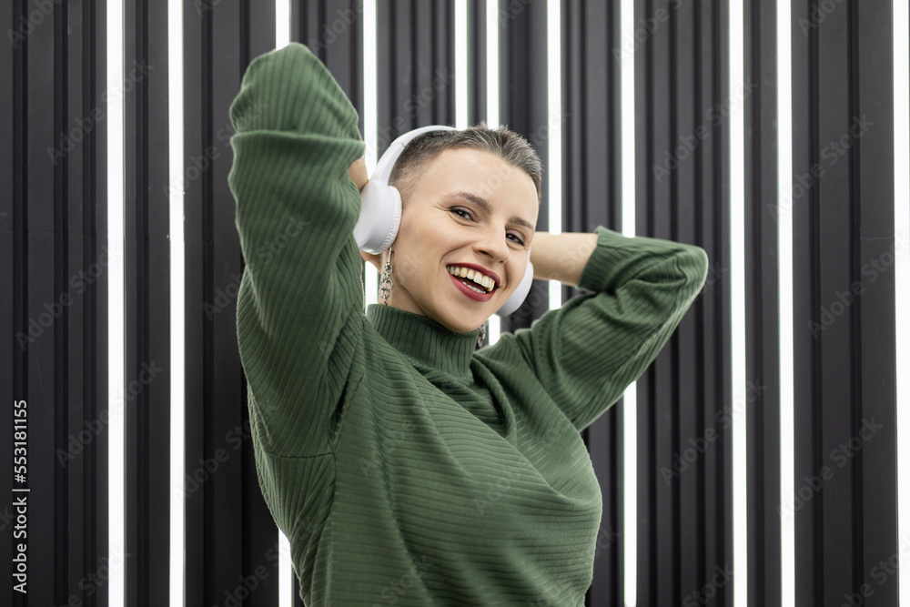 a stylish woman with a short haircut in headphones is dancing on the background of a gray wall with backlight a stylish woman with a short haircut in headphones is dancing on the background of a gray wall with backlight