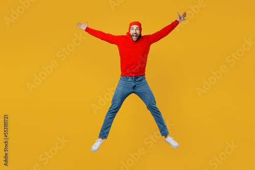 Full body exultant young caucasian man wear red hoody hat look camera jump high with outstretched arms hands scream isolated on plain yellow color background studio portrait. People lifestyle concept.