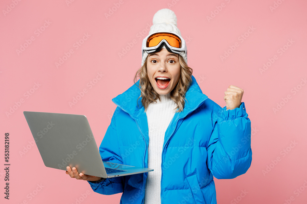 Snowboarder IT woman wear blue suit goggles mask hat ski padded jacket work use laptop pc computer do winner gesture isolated on plain pink background Winter extreme sport hobby weekend trip concept. Snowboarder IT woman wear blue suit goggles mask hat ski padded jacket work use laptop pc computer do winner gesture isolated on plain pink background Winter extreme sport hobby weekend trip concept.