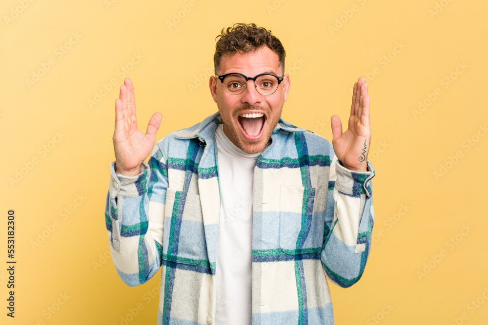 Naklejka premium Young caucasian handsome man isolated on yellow background receiving a pleasant surprise, excited and raising hands.