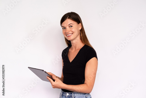 Portrait of happy young woman using digital tablet. Caucasian lady wearing black T-shirt and jeans working on touchpad and smiling. Wireless technology concept