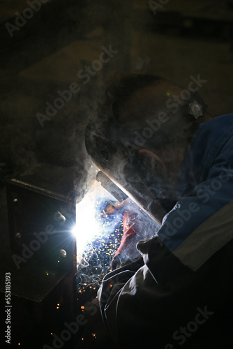 A worker welding metal parts on a construction site. A welder welds parts of a large machine in a metallurgical workshop.. An interesting example of manual work. © Cveja