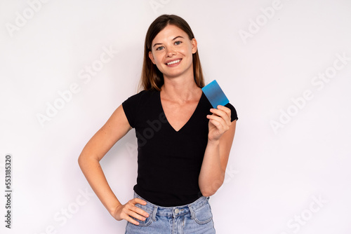 Portrait of happy young woman holding credit card over white background. Caucasian lady wearing black T-shirt and jeans advertising banking services. Cashless payment and banking services concept