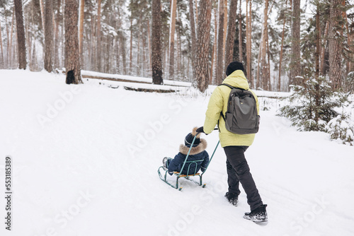 Happy teenager boy sledding and having fun outdoors. Joyful child playing in snow in winter forest. Laughing smiling kid walking in winter park in cold weather