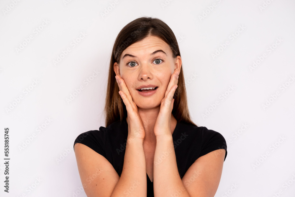 Portrait of excited woman looking at camera with open mouth over white background. Young Caucasian lady wearing black T-shirt and jeans touching face in surprise. Astonishment concept Portrait of excited woman looking at camera with open mouth over white background. Young Caucasian lady wearing black T-shirt and jeans touching face in surprise. Astonishment concept