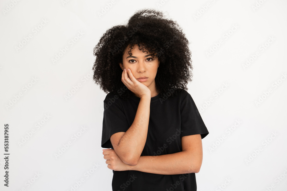 Displeased young woman holding hand on her cheek. Caucasian female model with afro hairstyle and brown eyes in casual clothes looking tired or uninterested listening to something. Boredom concept