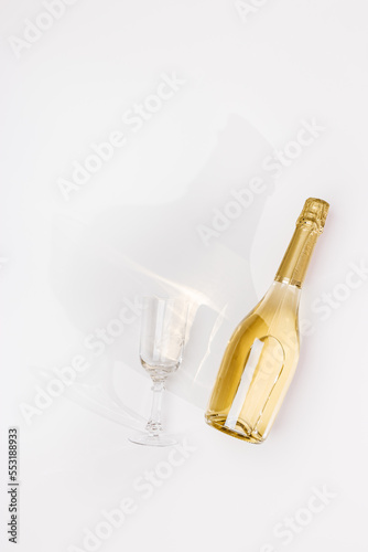 Top view white sparkling wine bottle and glasses wine with sun shadow and flare on light white background. Minimal aesthetic flat lay, golden champagne bottle. Summer alcohol drink concept