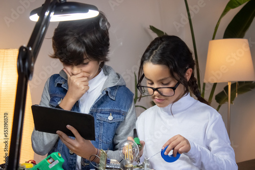 Serious school children creating new project on electronics. Cute girl soldering circuit board while boy thinking over results of experiment. Education, hobby concept