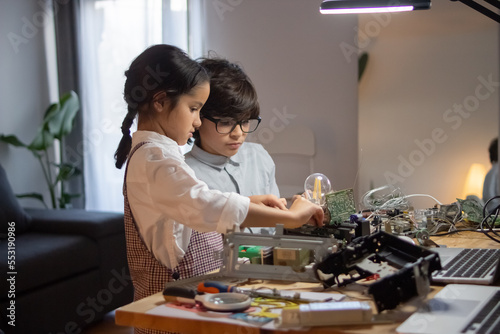 Side view of school children making robotics. Cute girl holding elements and wires while boy soldering circuit board. Education, hobby and robotics concept