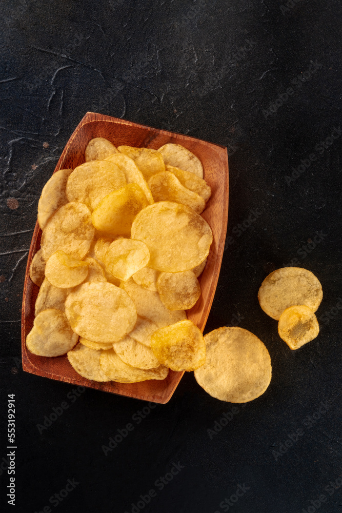 Potato chips in a wooden bowl, salty crisps, shot from the top on black with a place for text