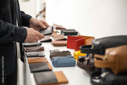 Craftsman hands laying out leatherwork on wooden showcase at leather workshop. Handwork accessories